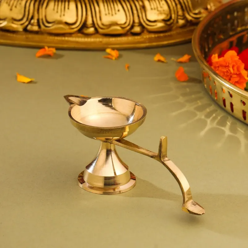 A brass pooja aarti diya with a handle, displayed against a decoration background.