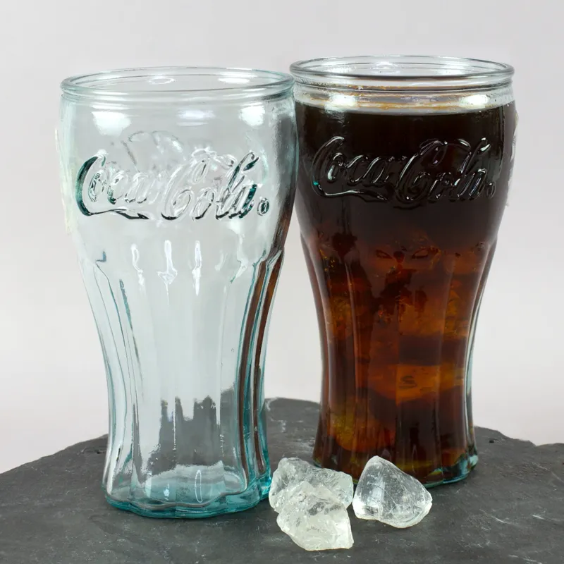 Retro Coca-Cola Glas aus 100 Prozent recyceltem Glas mit dunklem Getränk und leerem Glas auf Schieferplatte