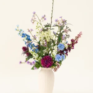 Eine weiße Vase mit dem künstlichen Seidenblumenstrauß „Purple Rain“ zeigt leuchtend violette und weiße Kunstblumen und grüne Blätter, ein Beispiel niederländischer Handwerkskunst vor einem hellen Hintergrund.