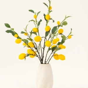 Eine weiße strukturierte Vase zeigt den künstlichen Seidenblumenstrauß „Lemons“ mit grünen Blättern und leuchtend gelben Zitronen vor einem hellen Hintergrund.