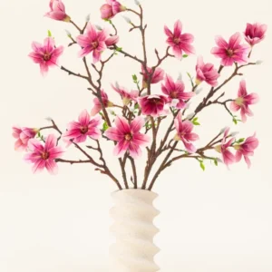 Der künstliche Blumenstrauß Magnolia Pink aus Seide ist in einer gewellten weißen Keramikvase mit grünen Knospen arrangiert und bildet eine elegante Präsentation vor einem hellen Hintergrund.