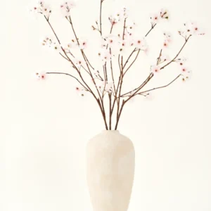 Der künstliche Seidenblumenstrauß Cherry Blossom Blush 114 cm hat hohe, zarte Zweige in einer schlichten beigen Vase, die Ihrem Interieur vor einem schlichten, hellen Hintergrund eine sanfte, elegante Note verleiht.