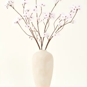 Der Seiden-Kunstblumenstrauß Kirschblüten hellrosa 114 cm steht in einer hohen beigen Keramikvase mit langen, dünnen Zweigen und zarten hellrosa Blüten und setzt einen ruhigen, künstlichen Blumenakzent vor einem schlichten Hintergrund.