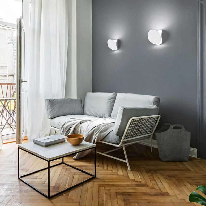 Moderne Wohnatmosphäre mit Shield LED Wandleuchte aus Metall über einem hellen Sofa und Couchtisch.