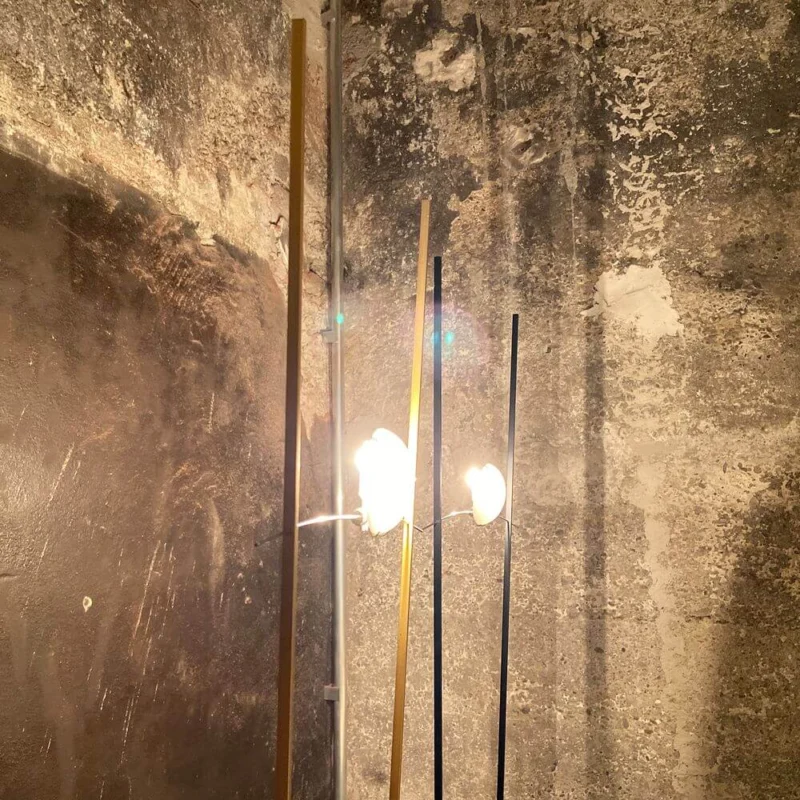 Ingo Maurer Stehlampe Ilios Designklassiker mit Opalglas und langen Metallstäben vor rauer Wand
