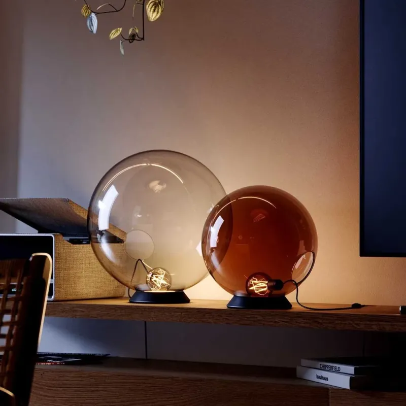 s.luce Orb Glaskugel Tischlampe auf einem Regal, minimalistisches Design mit zwei Glaskugeln und schwarzem Metallring.