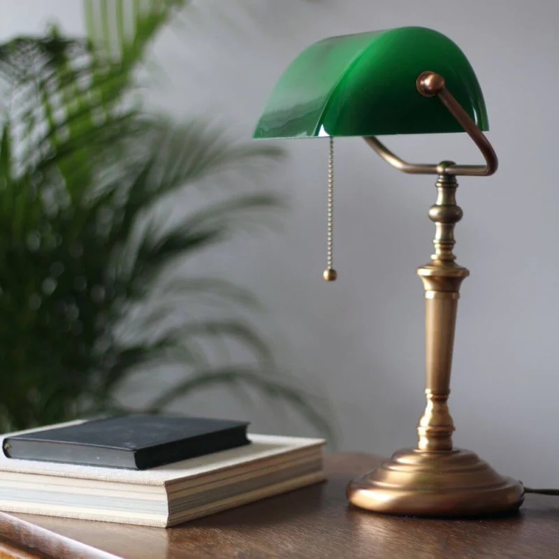 Vintage-Tischleuchte Ancilla Bankerslamp mit grünem Glasschirm und bronze-gebürstetem Fuß auf einem Tisch.