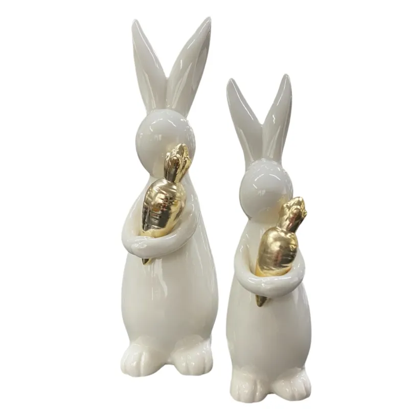 Zwei Deko Osterhasen aus creme-weißer Keramik mit goldener Möhre der Marke Formano
