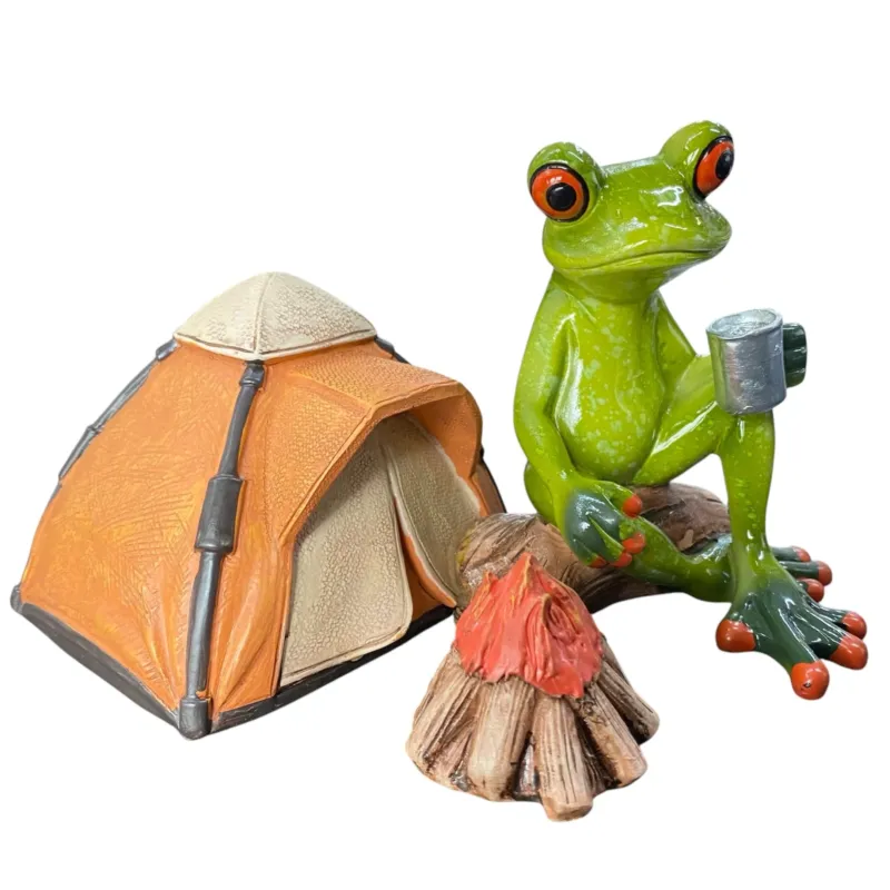 lustiger Deko Frosch sitzt am Lagerfeuer neben einem Zelt mit einem heißen Getränk in der Hand vor weißem Hintergrund