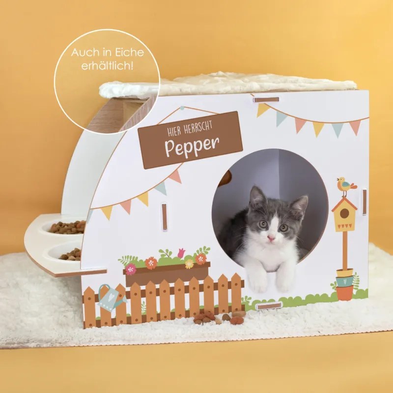 Weißes Katzenhaus mit Futterstation, Aufdruck Hier herrscht Pepper, Katzenbaby in der runden Öffnung und Hinweis auf Eiche-Variante