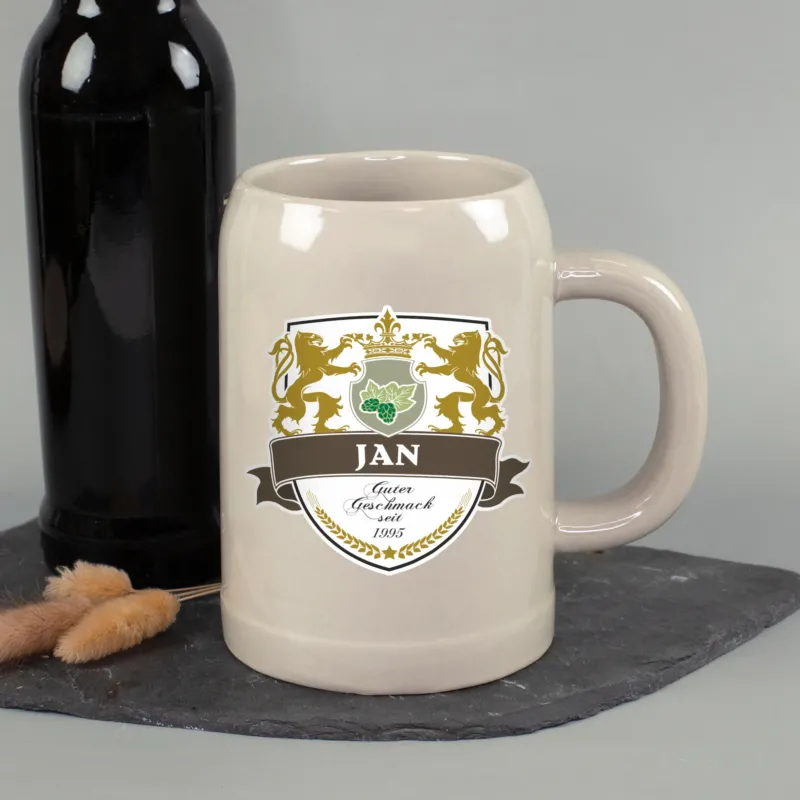 Personalisierter Steingut Bierkrug mit Name Jan und Wappenmotiv neben schwarzer Flasche auf Schieferplatte