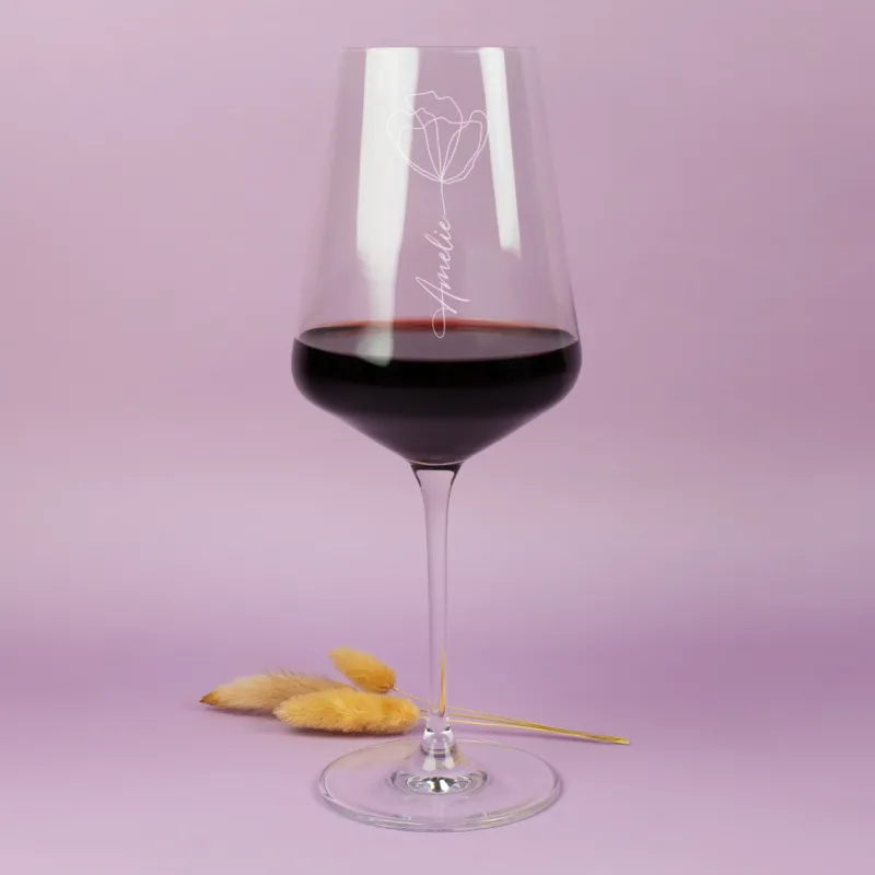 Elegantes Weinglas mit Gravur Name und Blumenmotiv mit Rotwein auf warmem Hintergrund