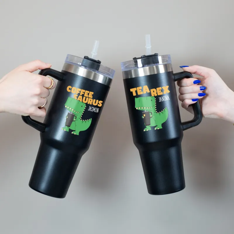 Beide Varianten des Thermobecher mit grünem Dino und orangem Schriftzug in Händen gehalten