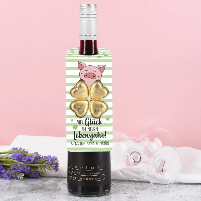 Flaschenanhänger mit grün-weißem Streifendesign, Kleeblättern, Glücksschwein und vier goldenen Lindt Schokoladenherzen, an einer Flasche befestigt.