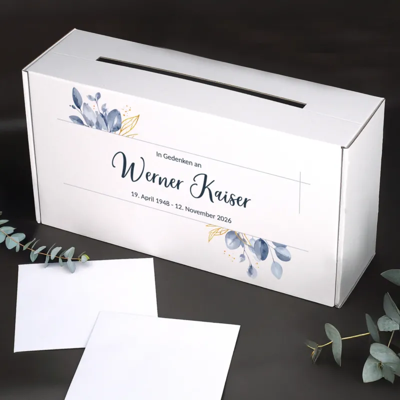 Personalisierte weiße Briefbox für Trauerfeiern mit Blattmotiv, Name und Datum, stabiler Karton, seitlicher Schlitz, dekoriert mit Eukalyptuszweigen.