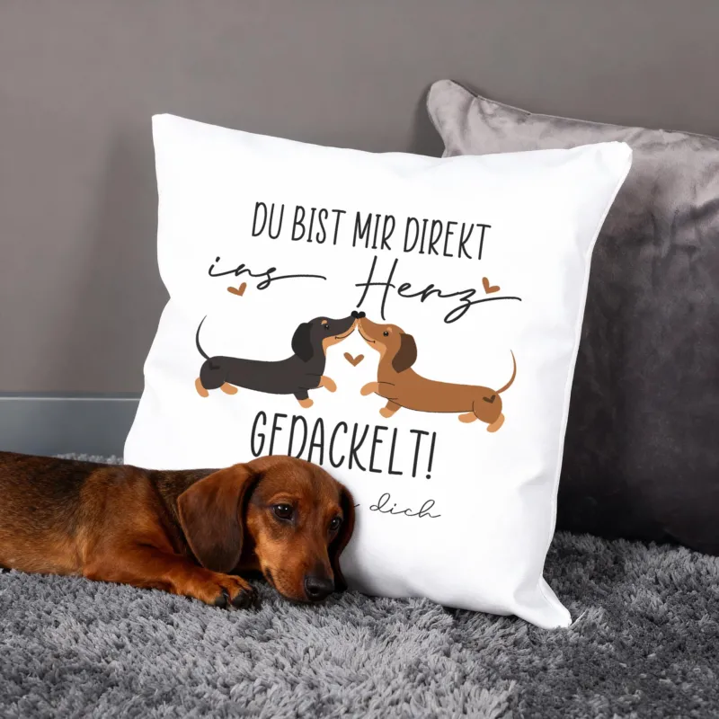 Personalisiertes Kissen mit Dackel-Pärchen und Spruch „Du bist mir direkt ins Herz gedackelt!“, Hund liegt davor