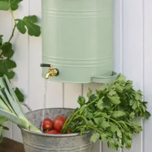 Wand-Wasserbehälter aus Metall in pastellgruen mit Messinghahn über Zinkwanne mit Tomaten und Kräutern.
